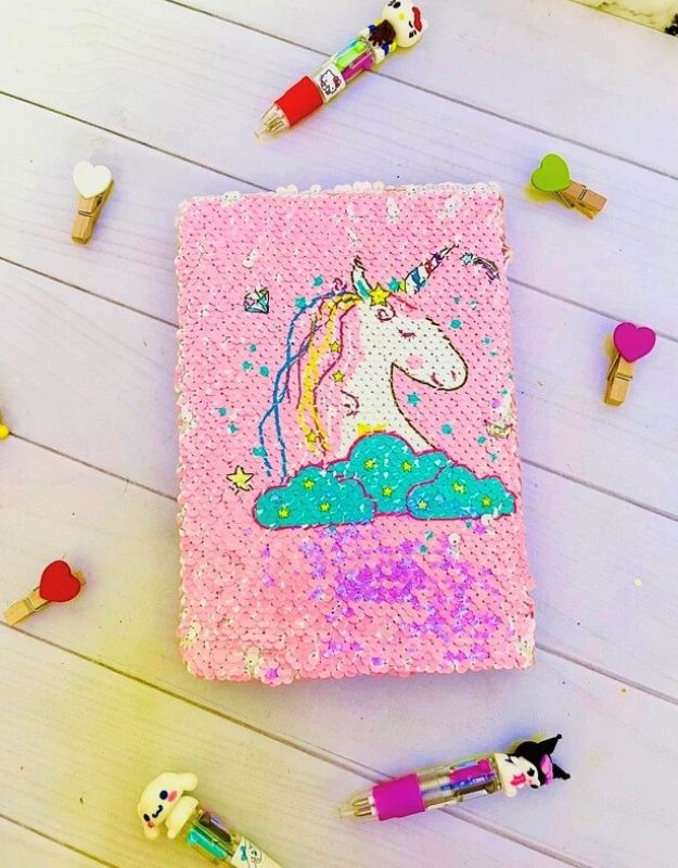 Pink notebook with unicorn design on a wooden surface with stationery items.